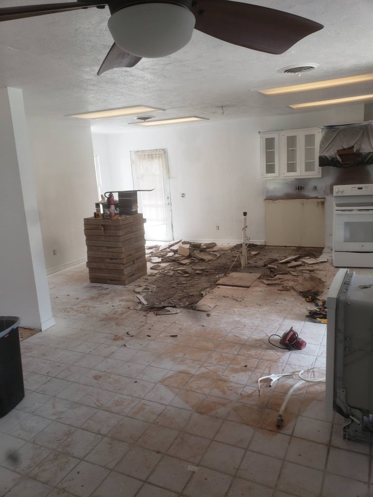 Kitchen before renovation with old floor tile torn up and debris on the floor