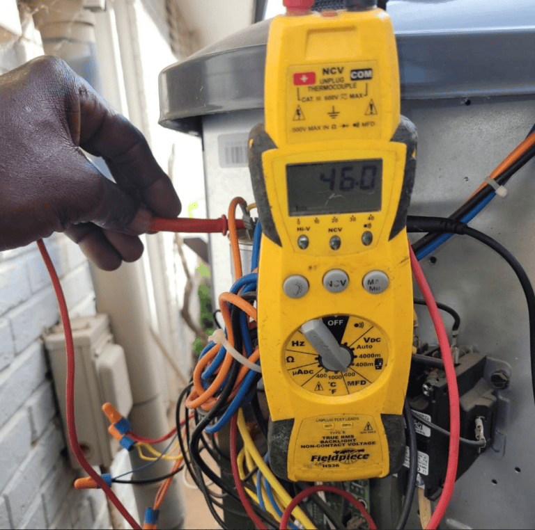 Technician testing the wiring of an outdoor AC unit with a yellow Fieldpiece clamp meter