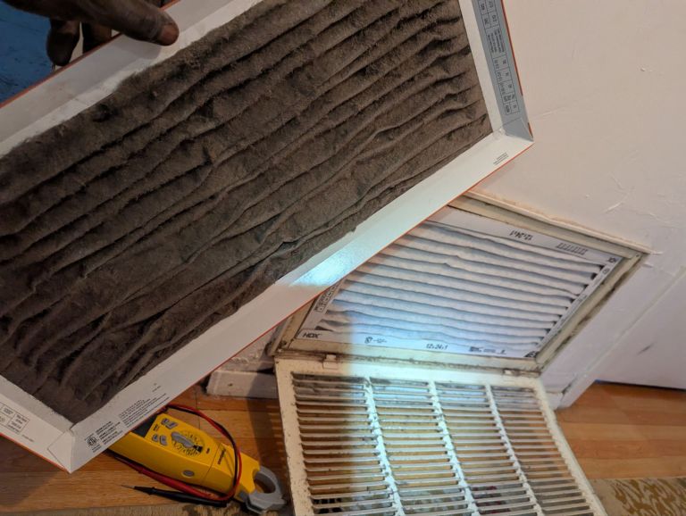 Dust-clogged HVAC air filter held beside an open return-air grille